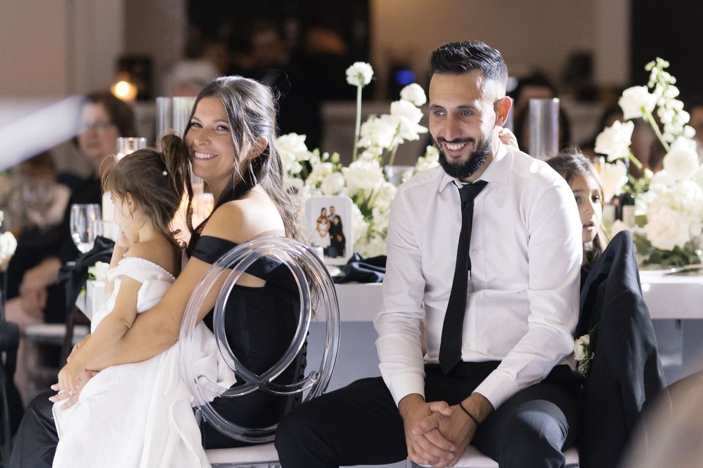 Wedding guests share a joyful moment during an elegant reception with white floral centerpieces and soft lighting.