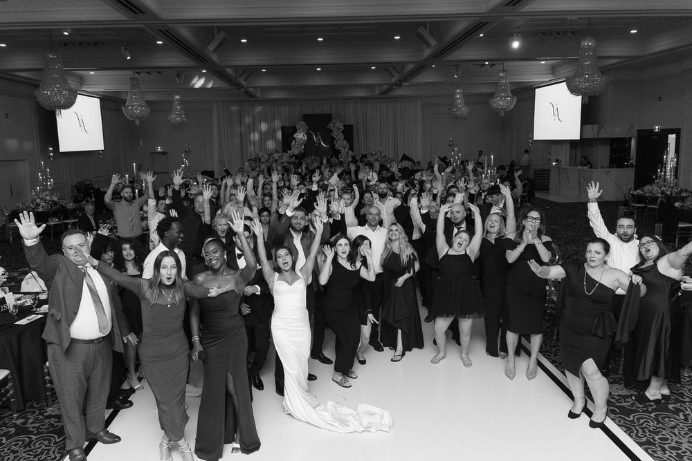 A black and white panoramic view of a crowded dance floor with people dancing and raising their hands in celebration.