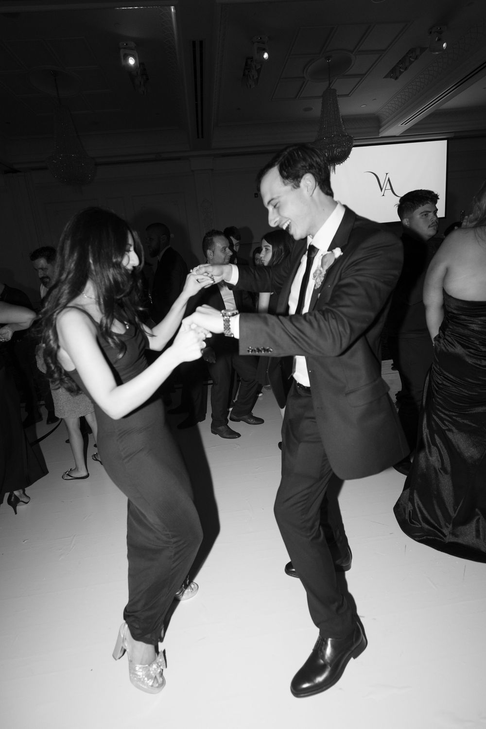 Black and white photo of wedding guests dancing energetically on the dance floor at a reception.