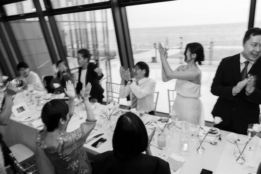 Black and white photograph of wedding guests celebrating and raising their glasses during a reception dinner.
