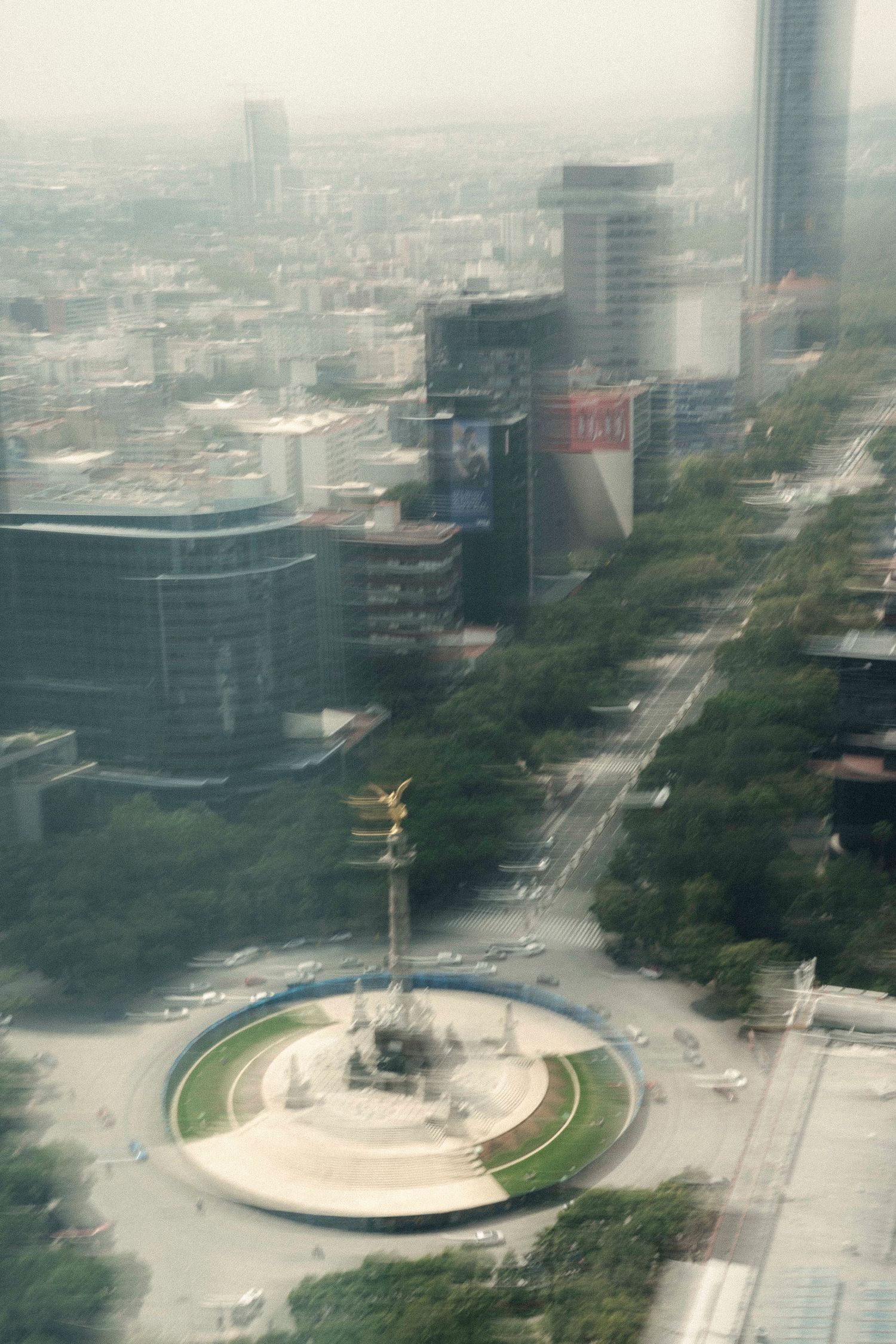 Aerial view of Mexico City's Angel of Independence monument surrounded by urban streets and modern buildings.