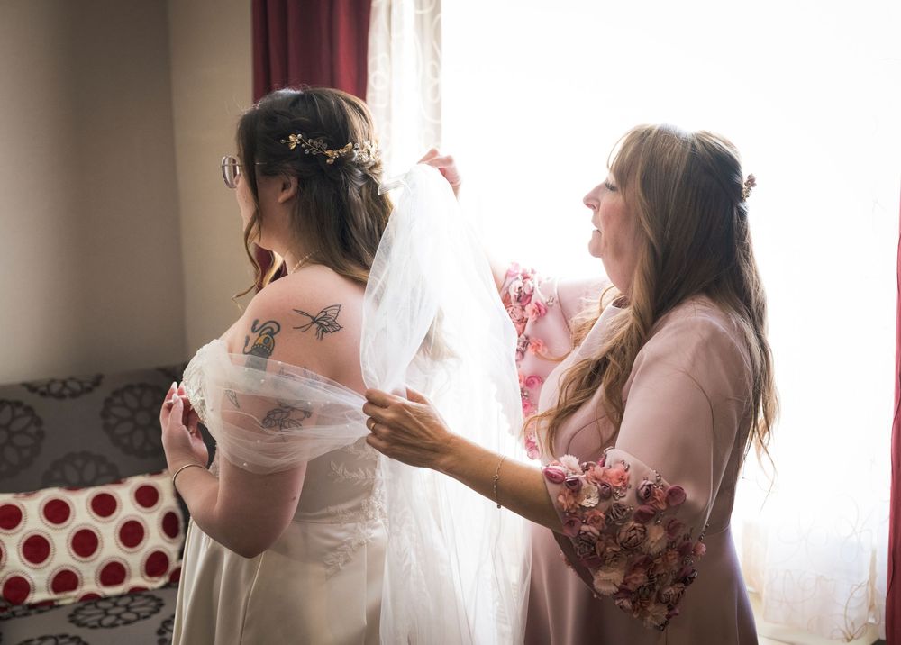 Wedding preparation scene showing final dress adjustments in a bright indoor setting.