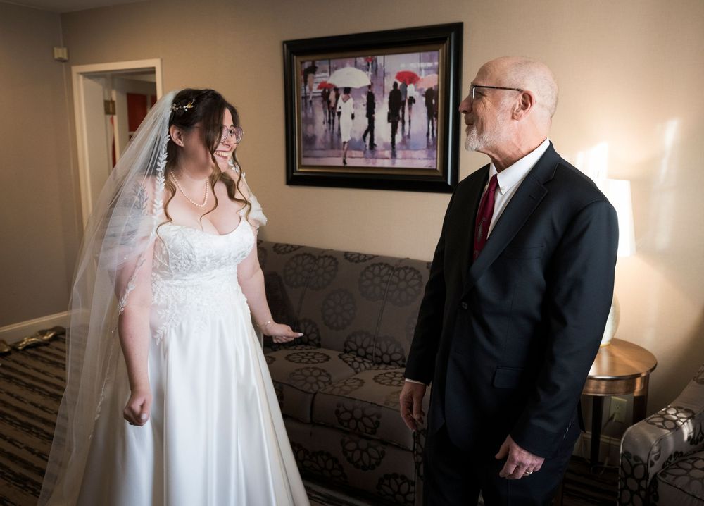 Wedding party members share candid interactions in a warmly lit indoor setting with framed artwork on the walls.