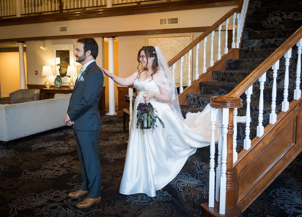 Couple poses on elegant wooden staircase with white railings during wedding photoshoot.