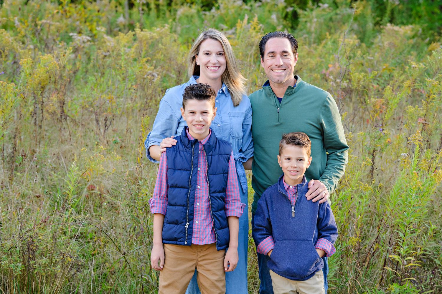 Family wearing coordinated blue and green outfits poses together during a portrait session in Ohio in a wildflower meadow during autumn.