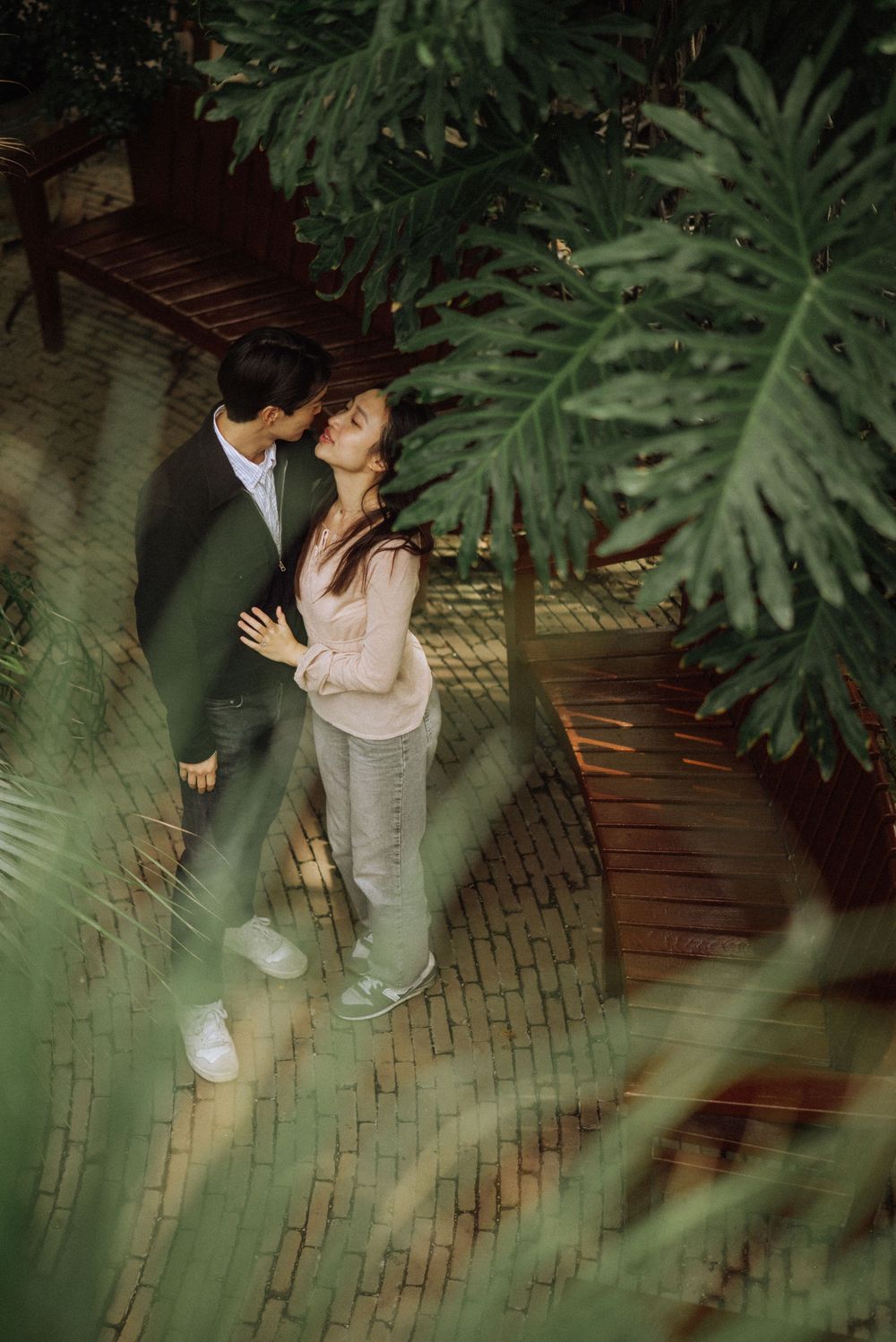A couple embraces in a tropical garden setting with large monstera leaves in the foreground.