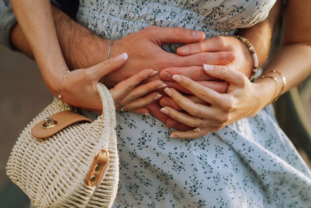Close-up of hands holding white woven handbag against floral dress.