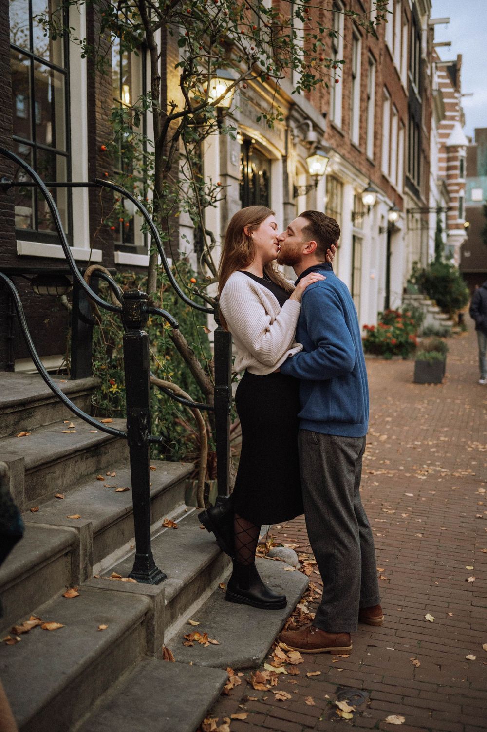 A romantic couple shares an intimate moment on a brick-lined street during autumn.