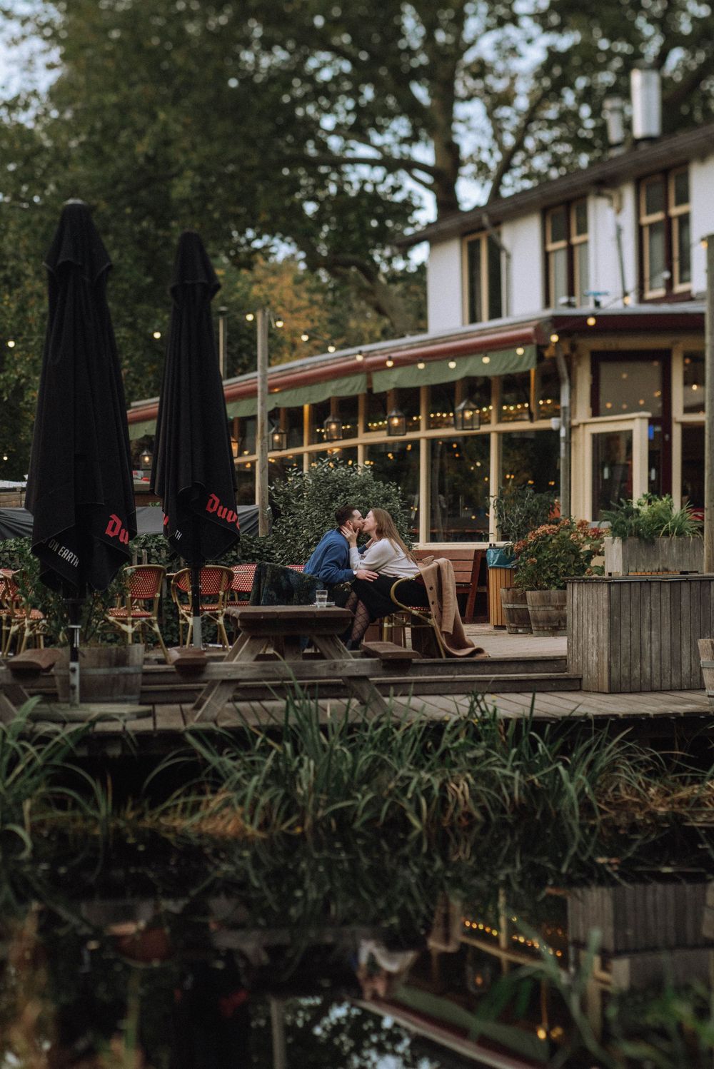 A waterfront restaurant terrace with string lights and umbrellas at dusk.
