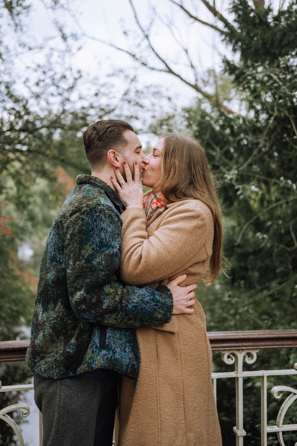 Couple embracing on bridge during autumn with trees in background.