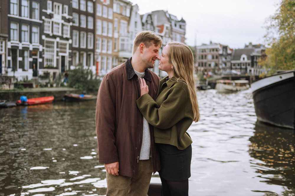 A couple stands along Amsterdam's iconic canals with historic buildings in the background.