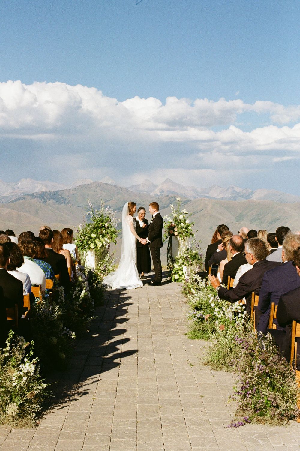 Mountain wedding ceremony setup with white floral decorations and guests seated against a scenic backdrop.