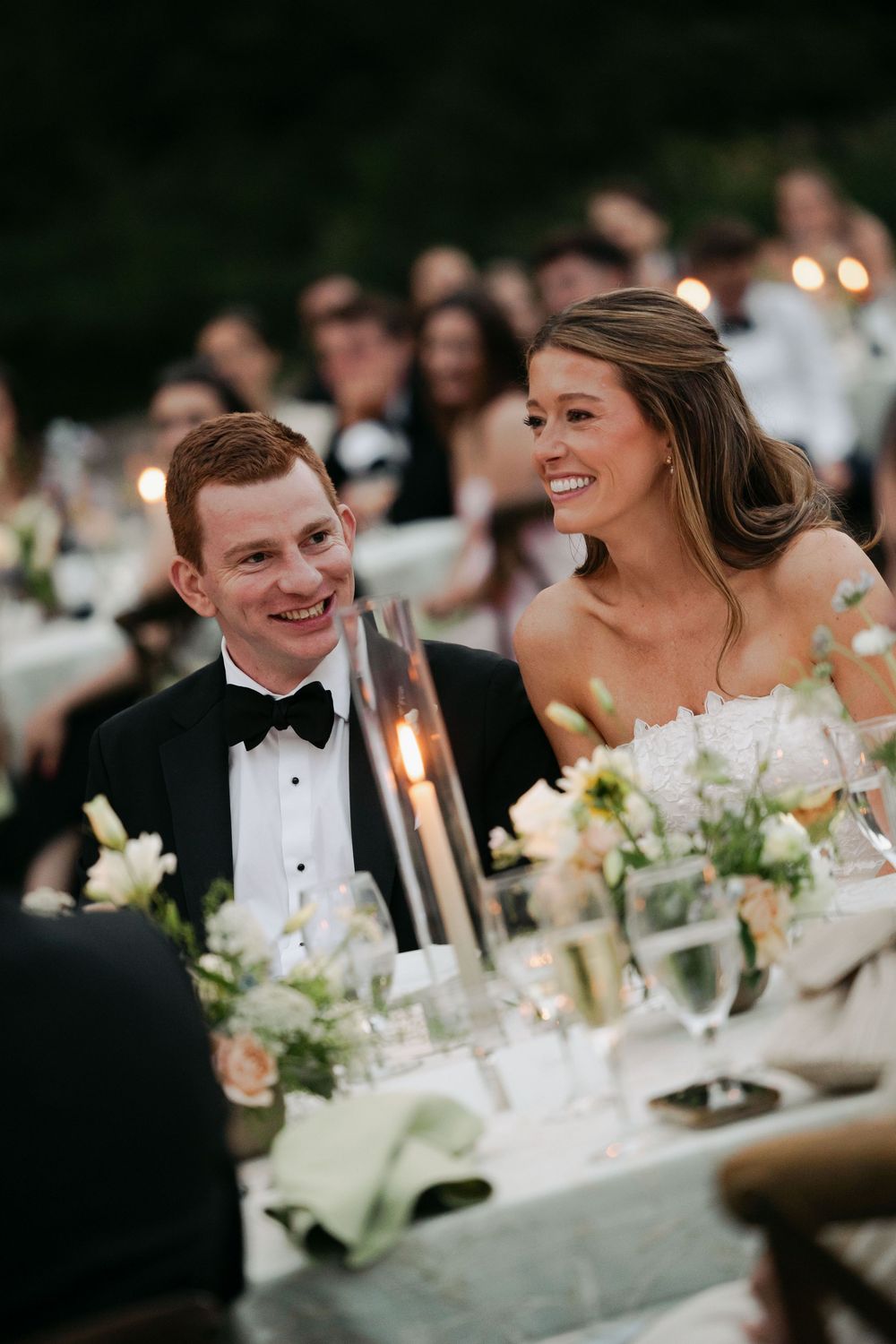 Wedding reception dinner table with elegant white floral centerpieces and candlelight settings.