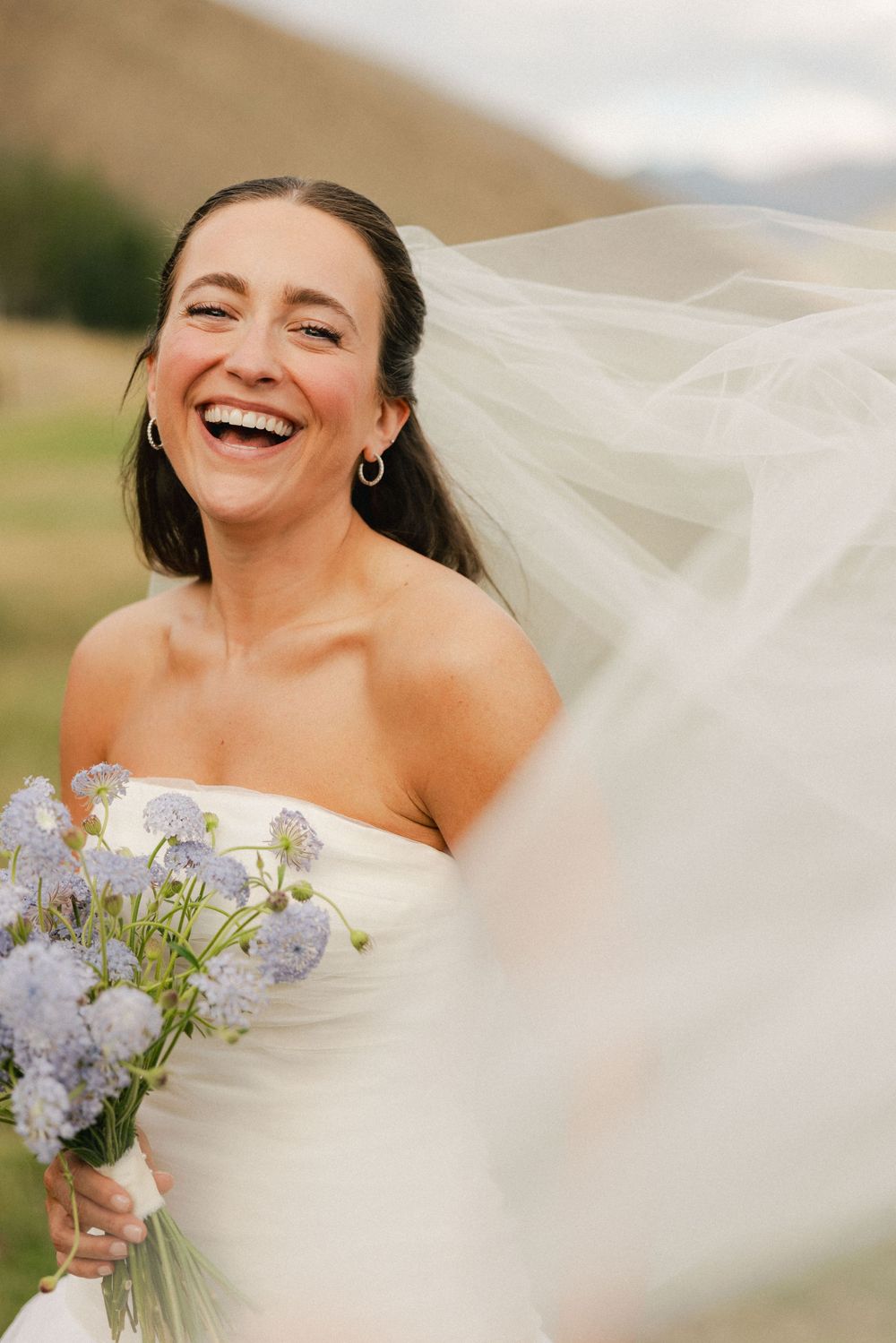 Joyful moment captured with flowing veil and delicate purple flowers in sunlight.