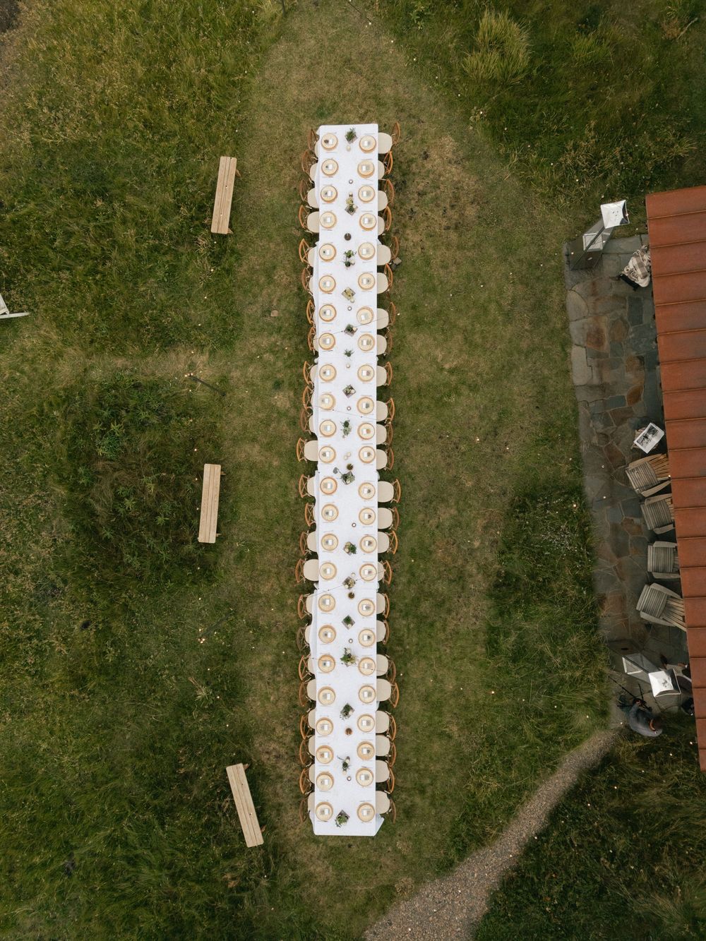 Aerial view of a long white dining table set up outdoors on grass.