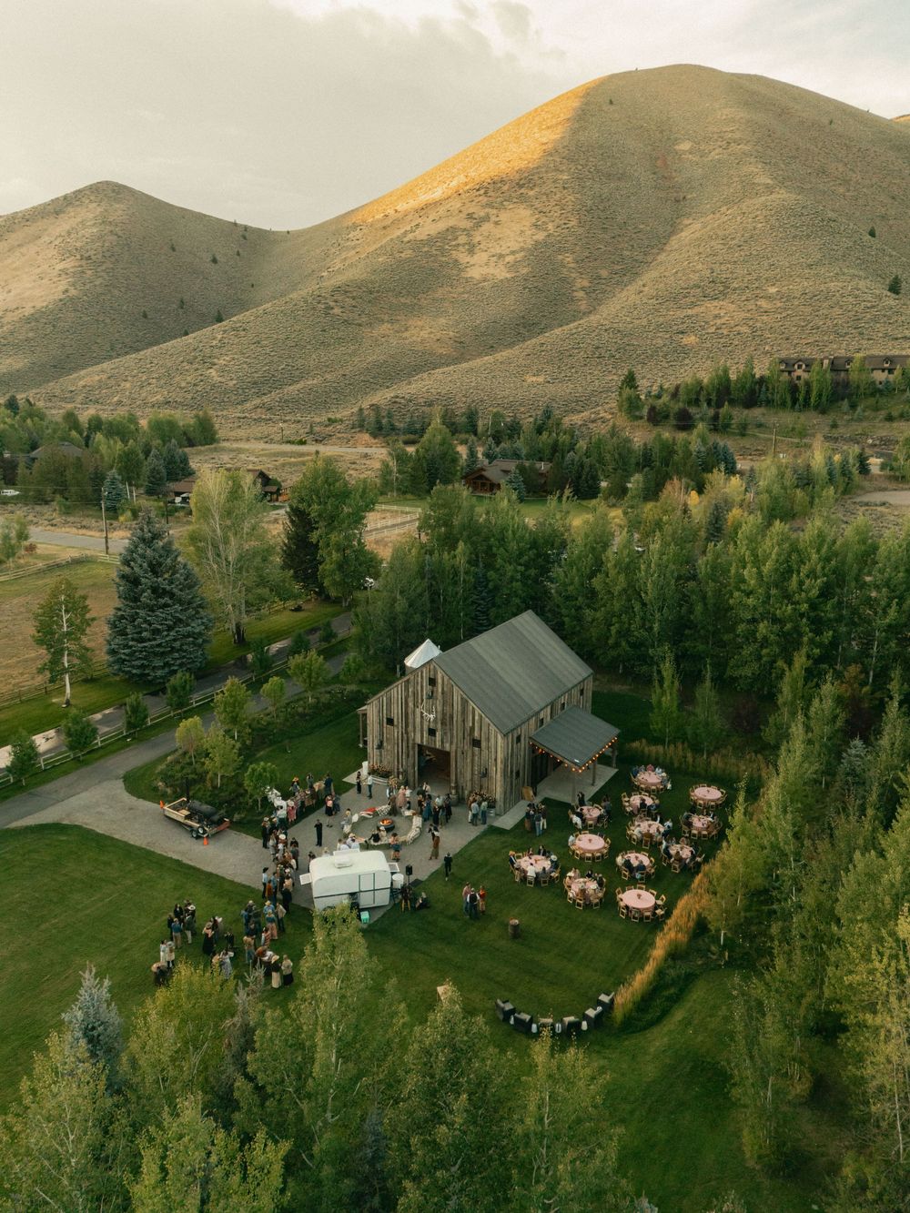 Aerial view of an outdoor wedding venue nestled in mountains with guest seating and reception area.