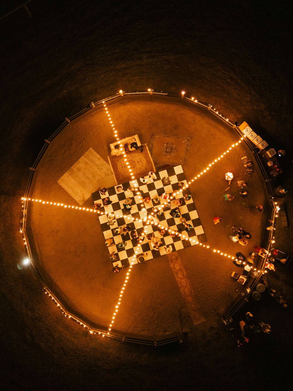 Aerial view of glowing candles arranged in a cross pattern on the ground at night.