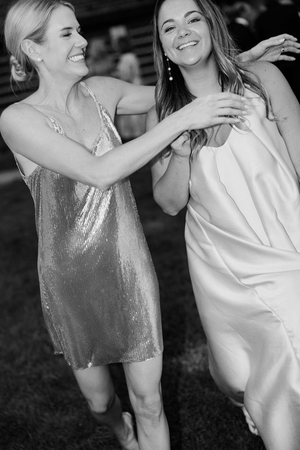 Two women dancing and celebrating in sparkly and white dresses at a party.