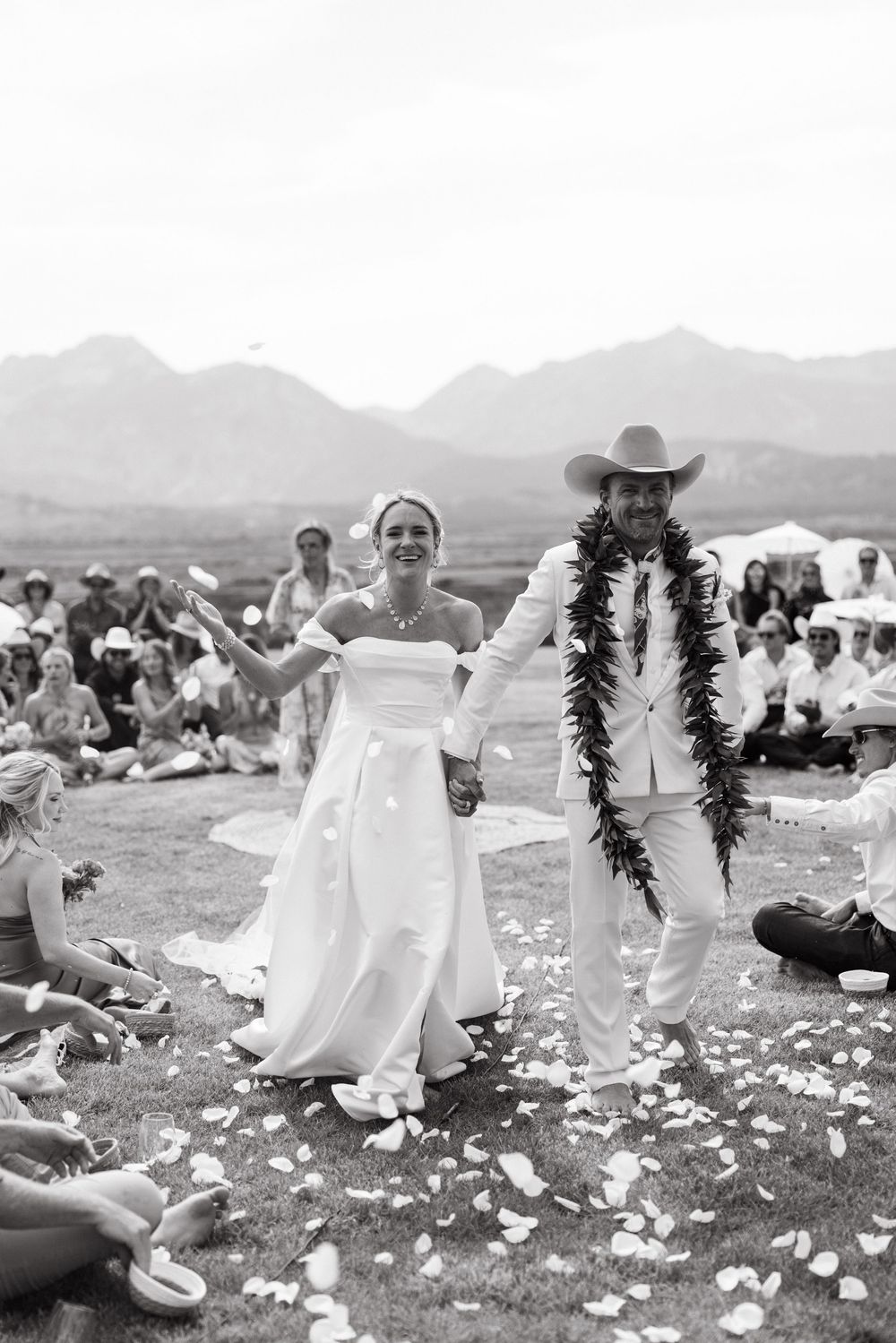 Black and white photo series of a joyful outdoor wedding celebration with guests sitting in a meadow against mountain views.