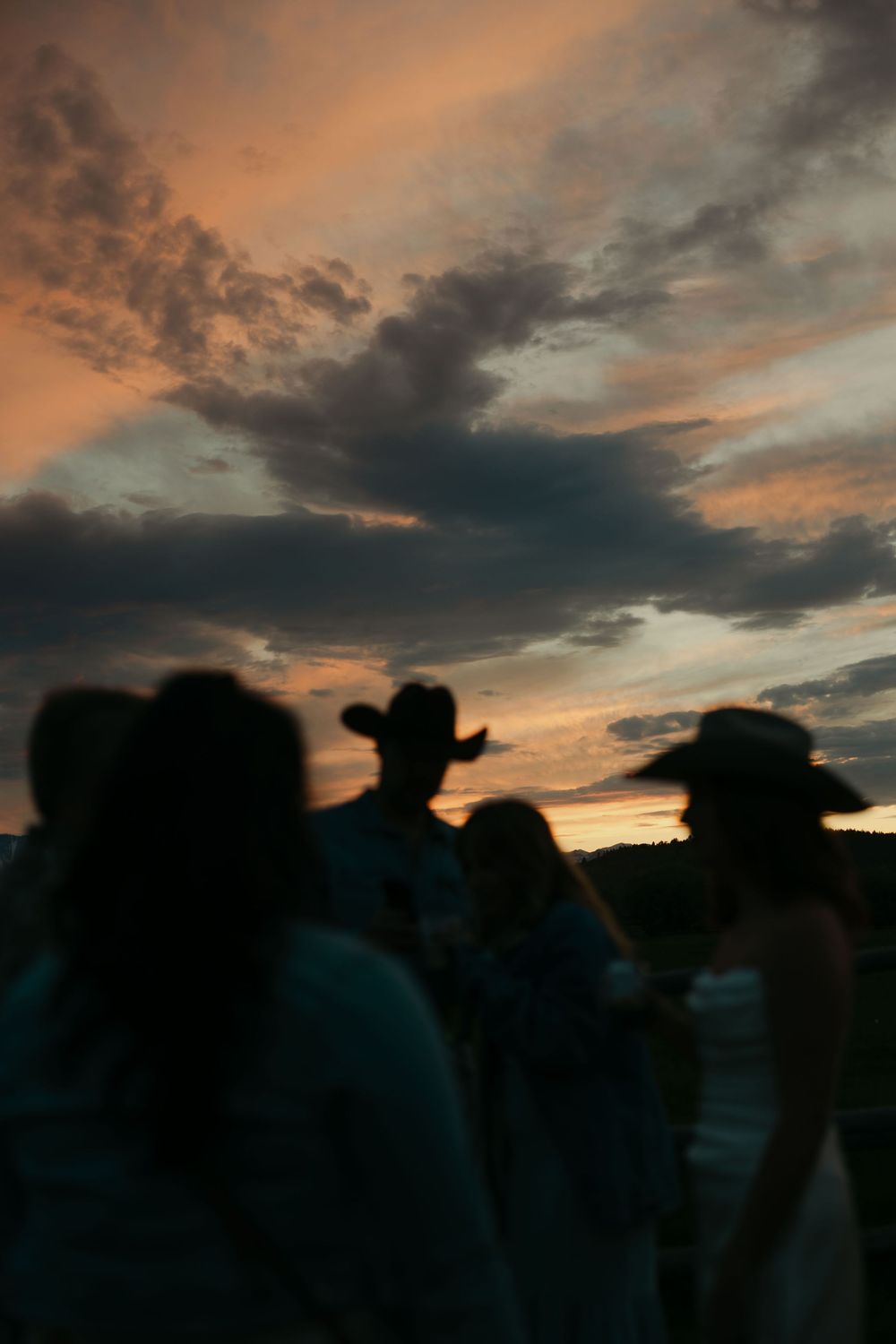 Silhouettes of people wearing cowboy hats gathered outdoors against a dramatic orange and blue sunset sky.