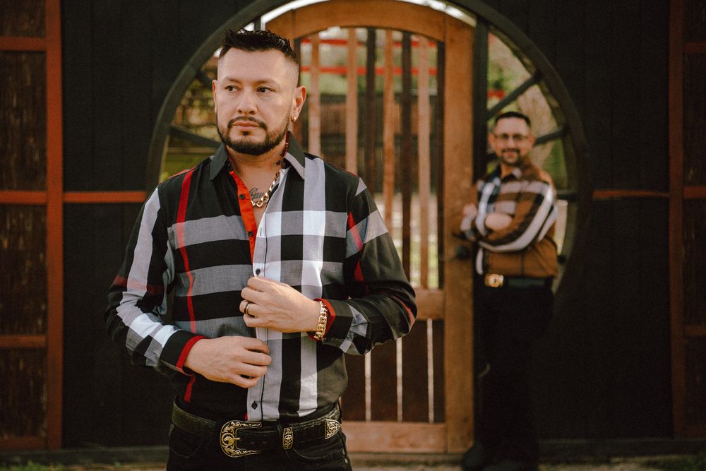 Person wearing a black and white checkered shirt holds a dark bottle while standing in a rustic wooden interior.