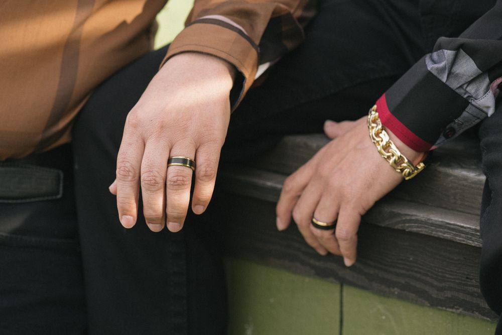 Close-up shot of two hands wearing wedding rings resting on a dark surface.