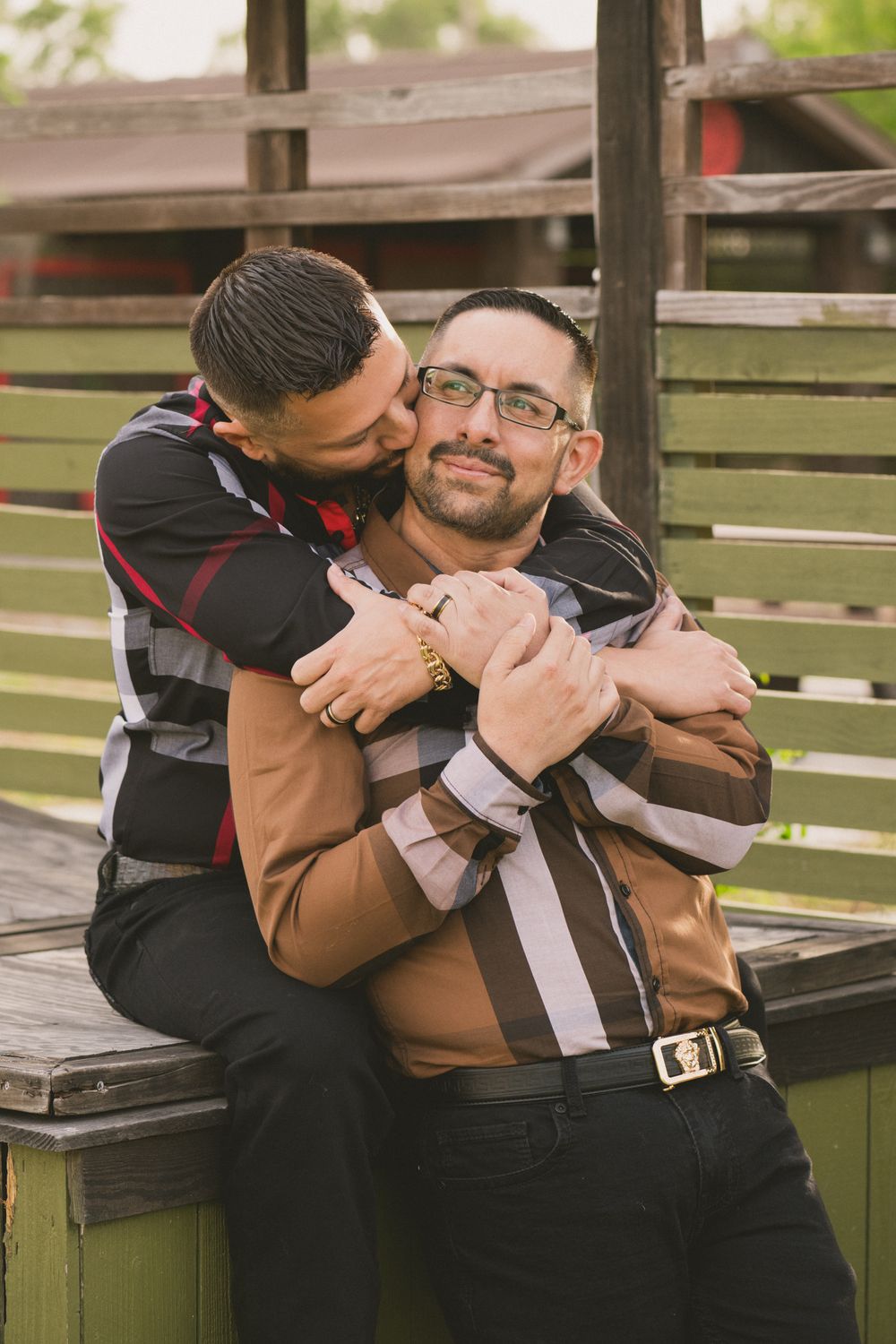 Two people share an affectionate embrace while sitting on wooden benches in an outdoor setting.
