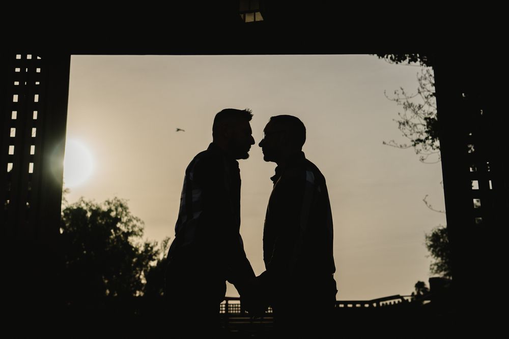 Romantic silhouettes of two people sitting close together on a bench at sunset.