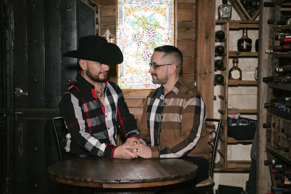 Two people in dark attire sit at a rustic wooden table in a cozy cabin-like setting.