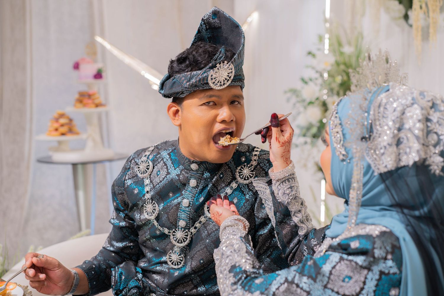 Couple in traditional attire sharing a moment while looking at a phone during a celebration.