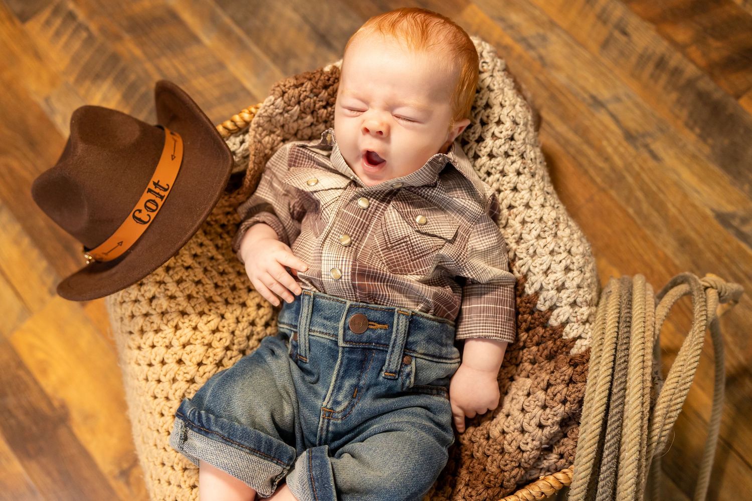 Baby in denim overalls sleeping peacefully on wicker furniture with wooden floor background (Faison, NC).