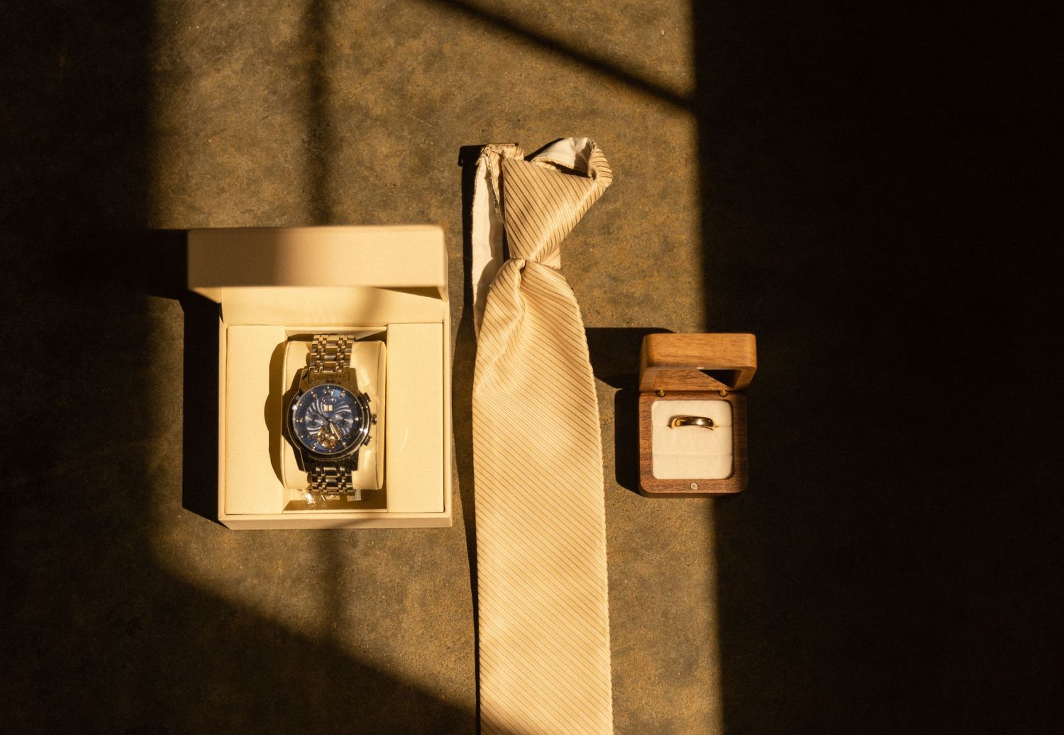 A watch and ring box arranged with a gold tie in dramatic lighting.
