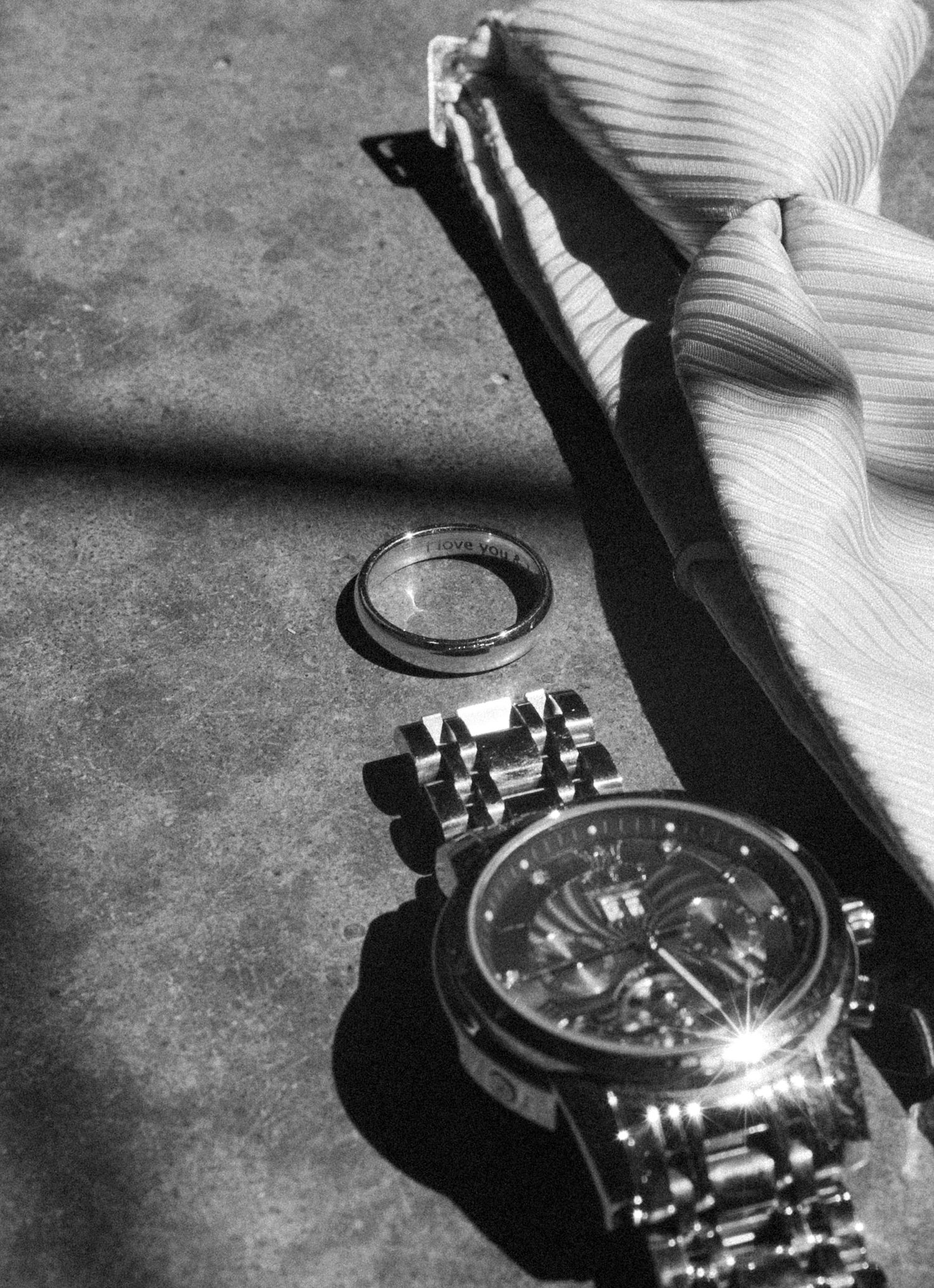 A luxury chronograph watch and ring casting dramatic shadows on a textured surface.