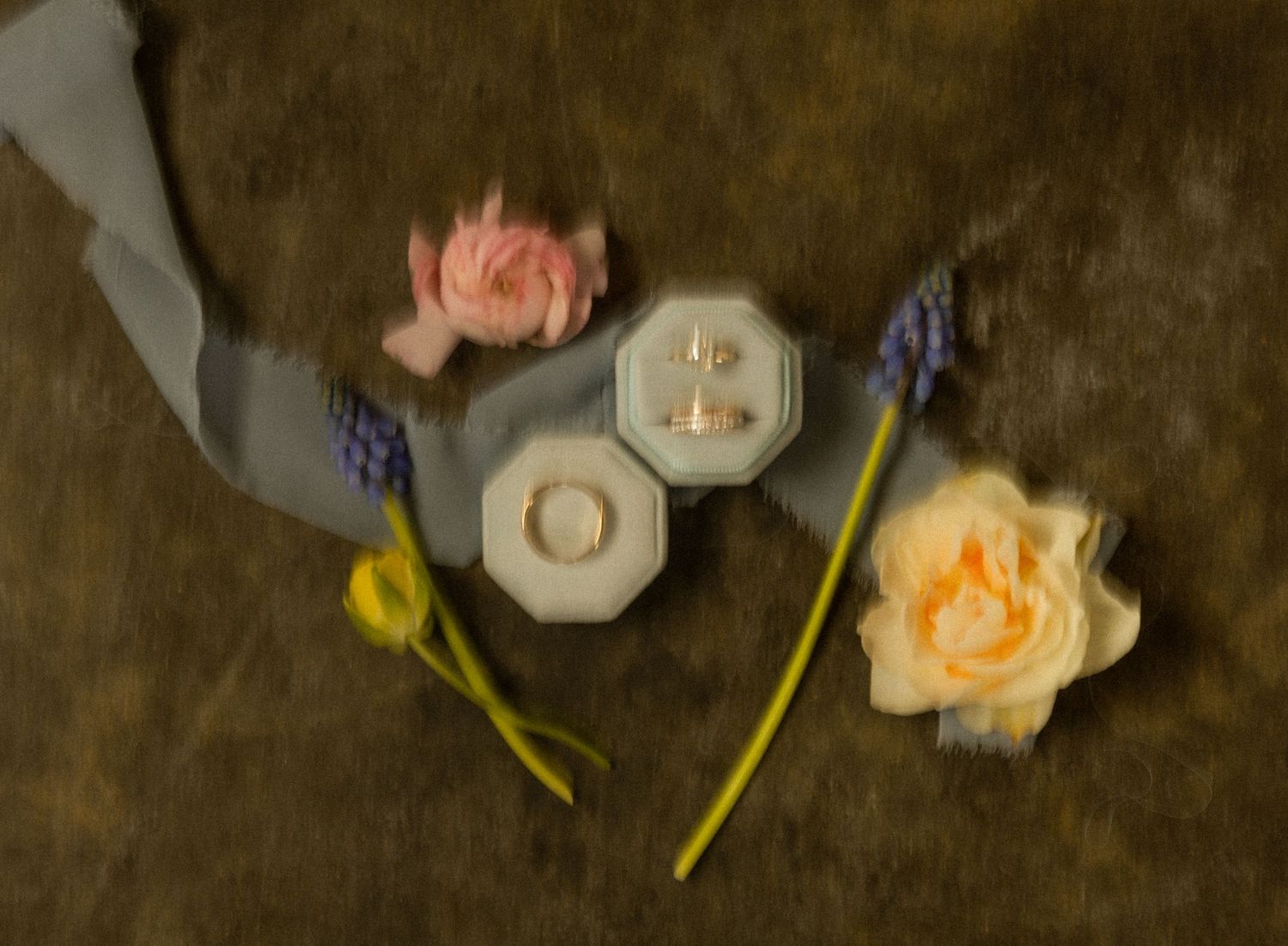 Delicate flowers and ring boxes arranged artistically on a dark textured surface.