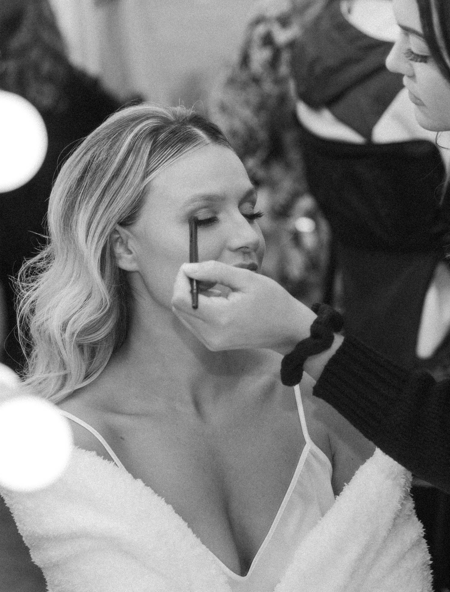 A black and white getting-ready photo shows final makeup touches being applied.