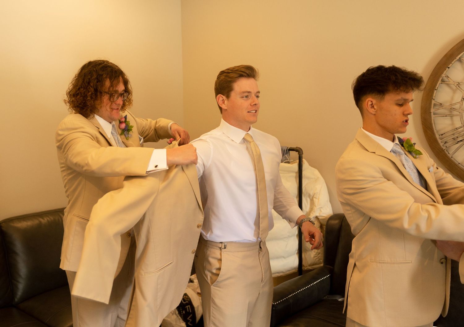 Groomsmen help with final preparations in a beige-toned room.