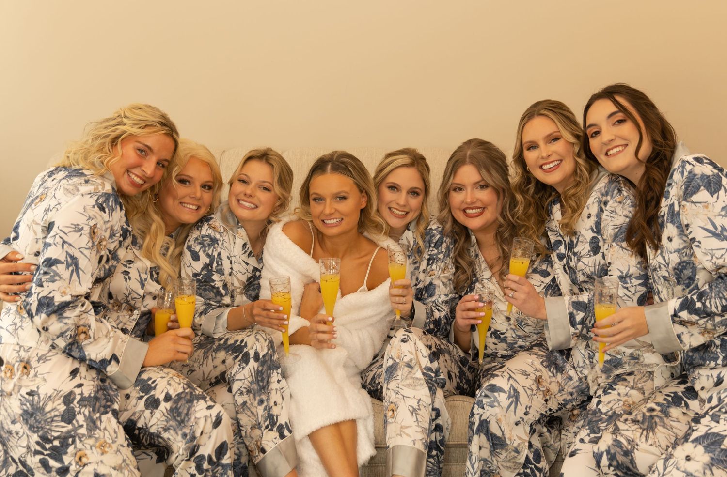 Bridesmaids in floral print dresses gather for a celebratory photo with drinks.