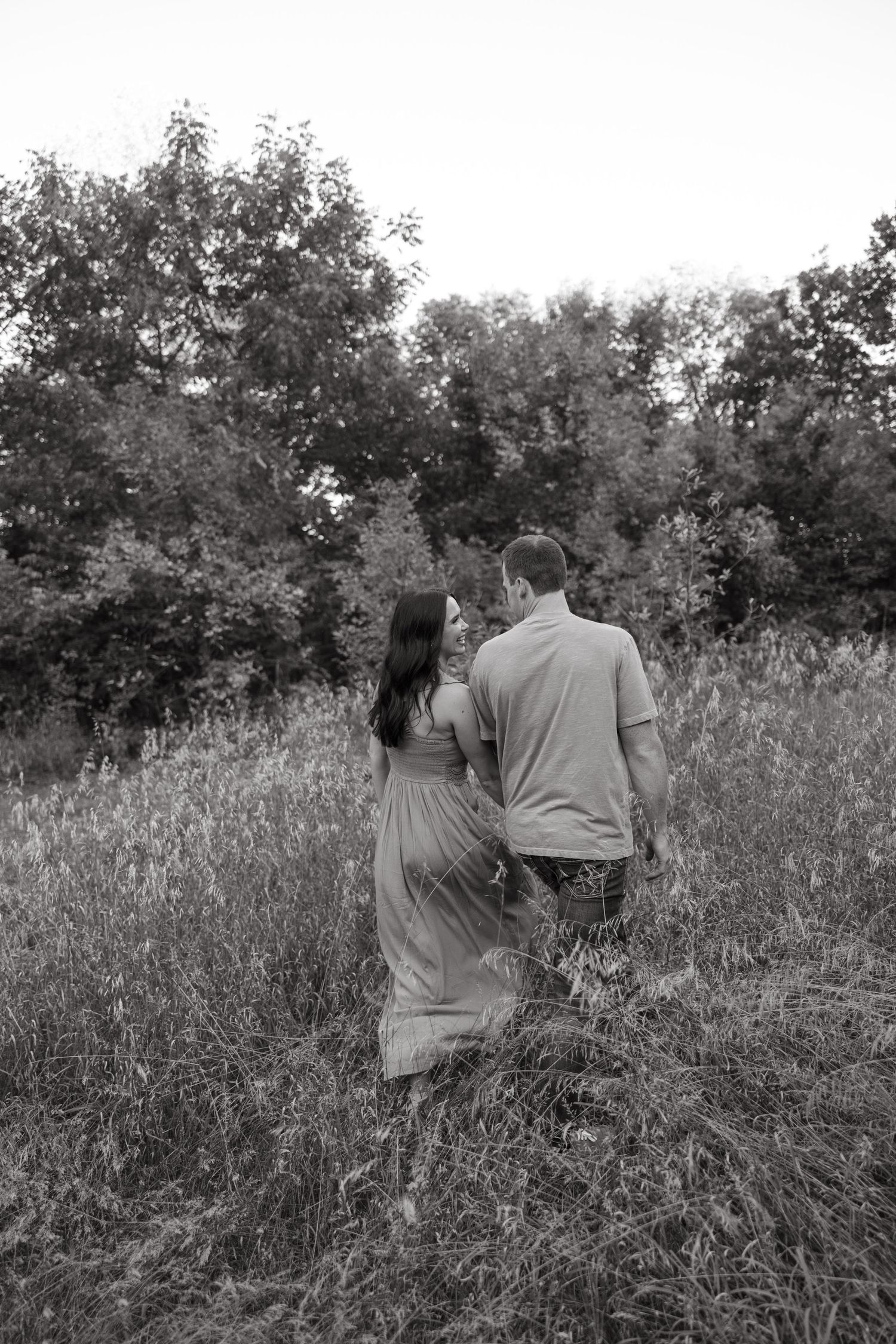 Couple walking through tall grass field in black and white photography.