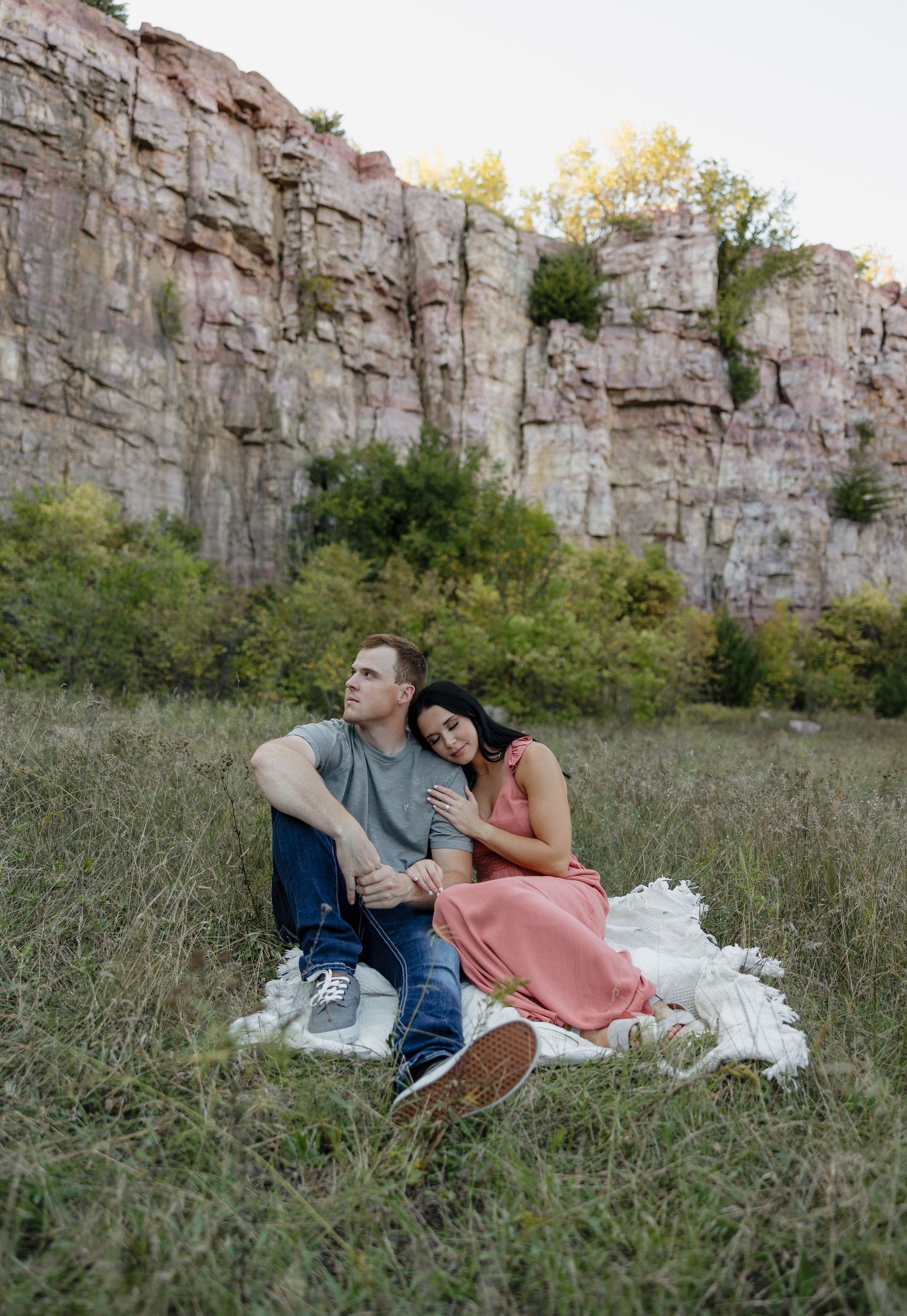 Couple relaxing on blanket near towering limestone cliffs in natural setting.