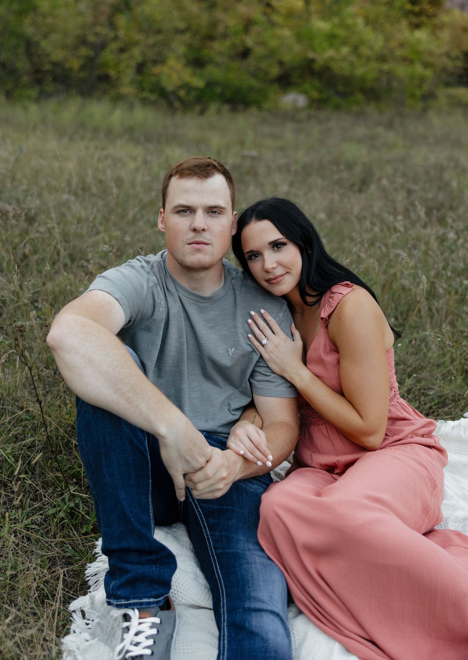 Intimate outdoor portrait session with couple sitting on white blanket in grassy field.