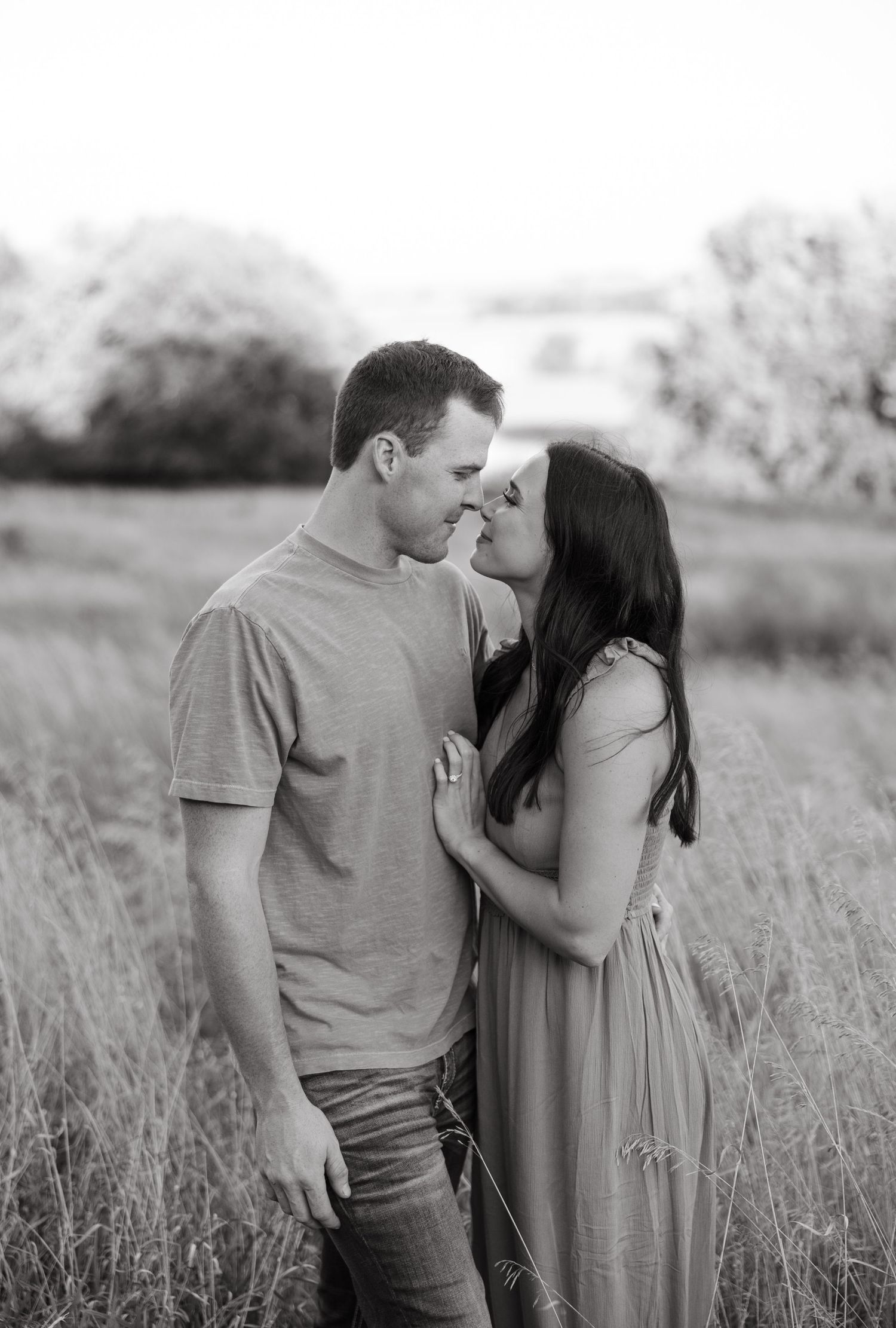 Black and white romantic portrait of couple in embrace among tall grass.