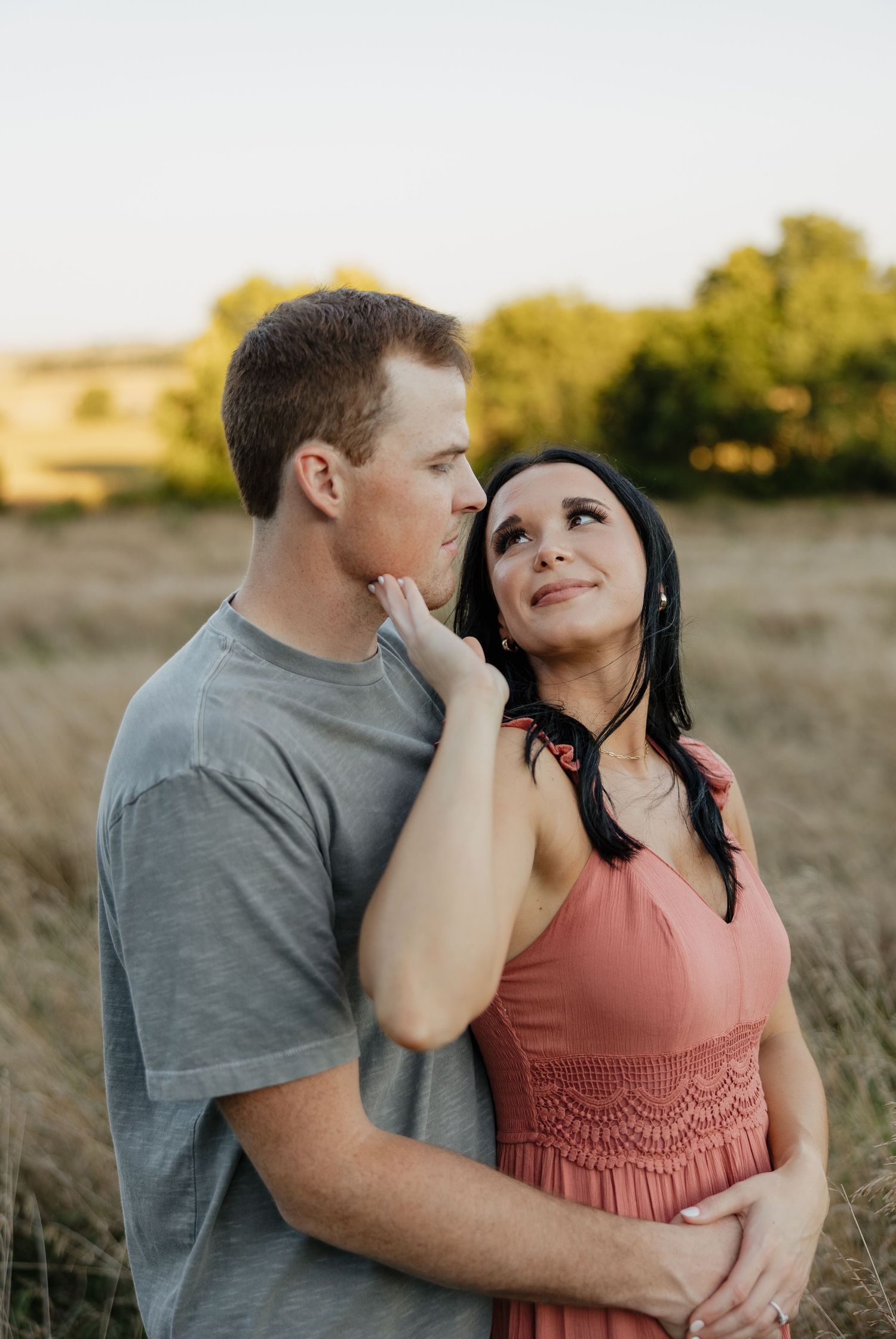 A tender moment between a couple in casual clothing against a sunset backdrop.