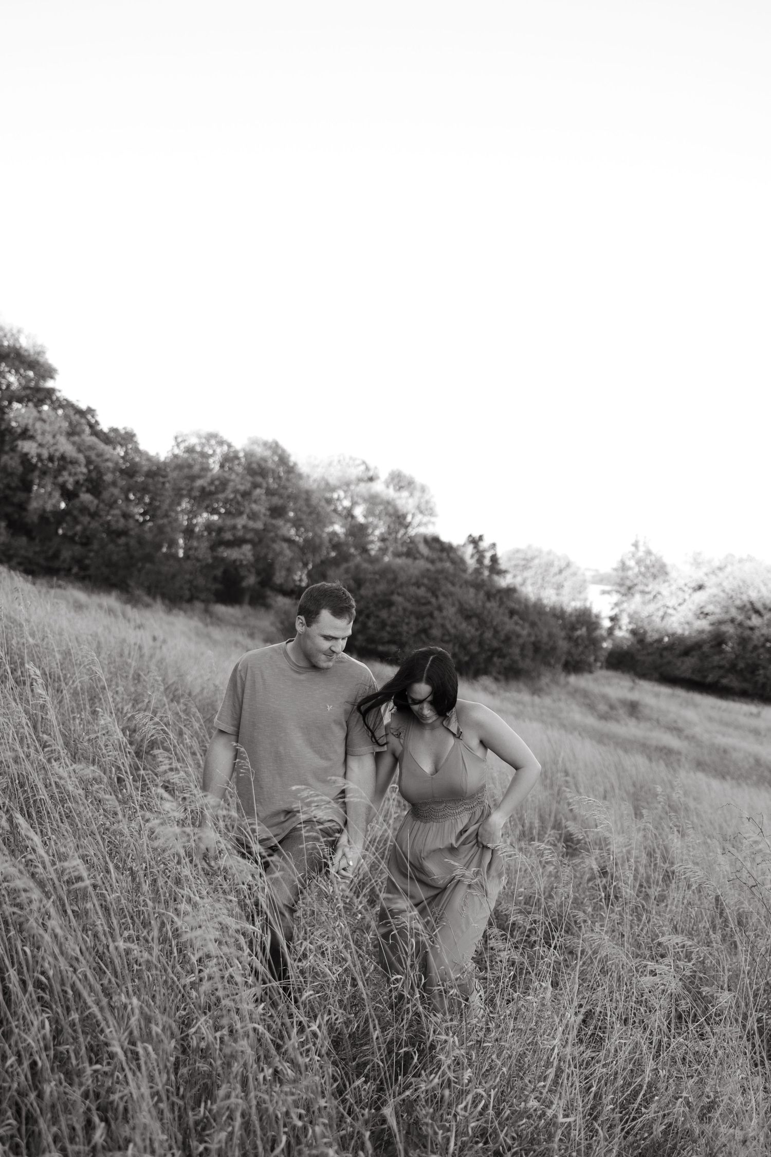 A couple explores a field with tall grass at golden hour in black and white.