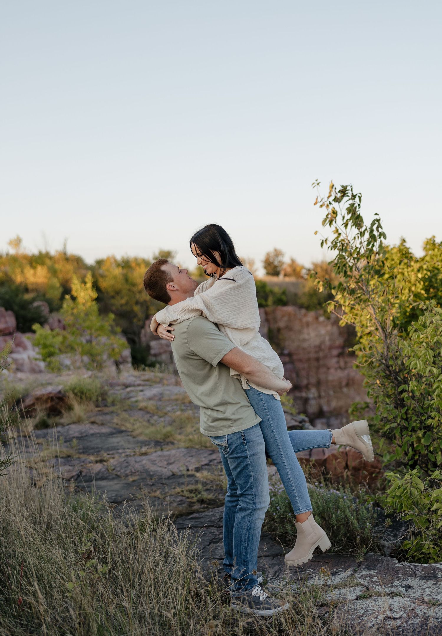 A couple shares a playful moment as one gives the other a piggyback ride against a scenic natural backdrop.