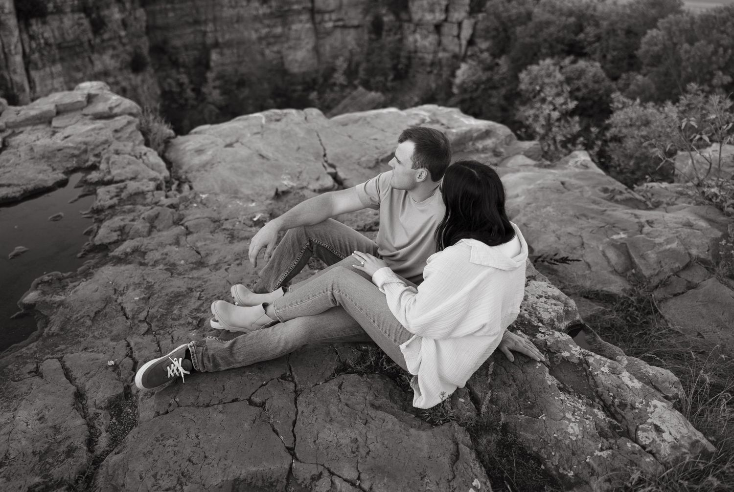 A couple relaxes together on rocky terrain in a black and white photograph.