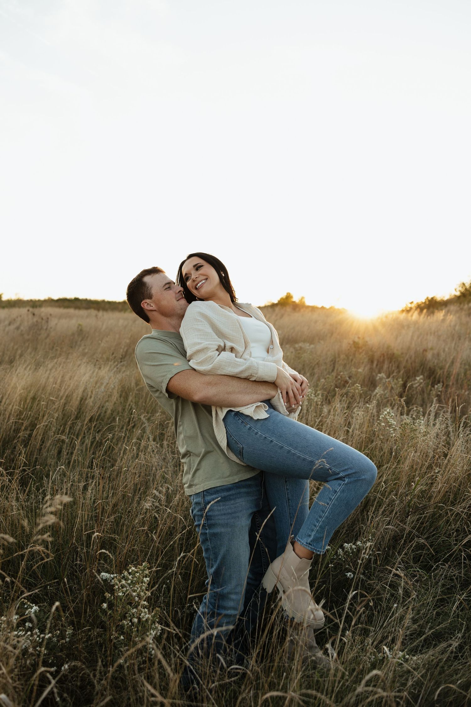 A couple shares an intimate moment while standing in tall grass during golden hour.