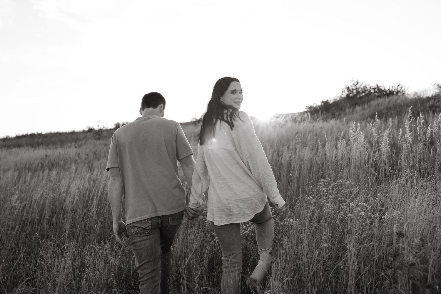 A black and white photo captures a couple walking through a meadow of tall grass.