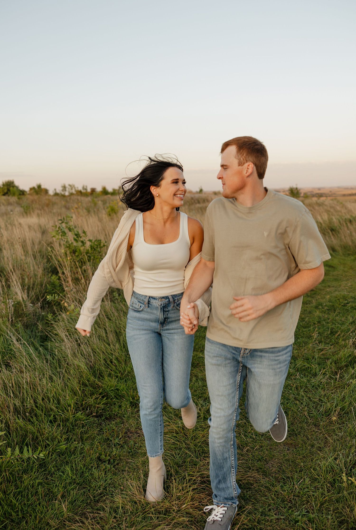 A joyful couple runs together through a grassy field at sunset.