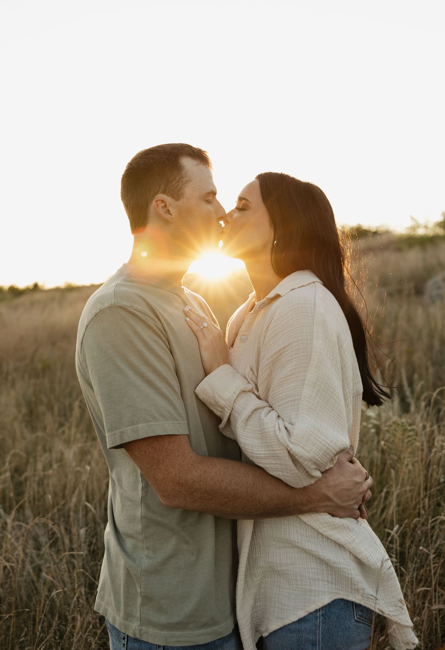 Couple sharing romantic kiss during golden hour sunset in field.