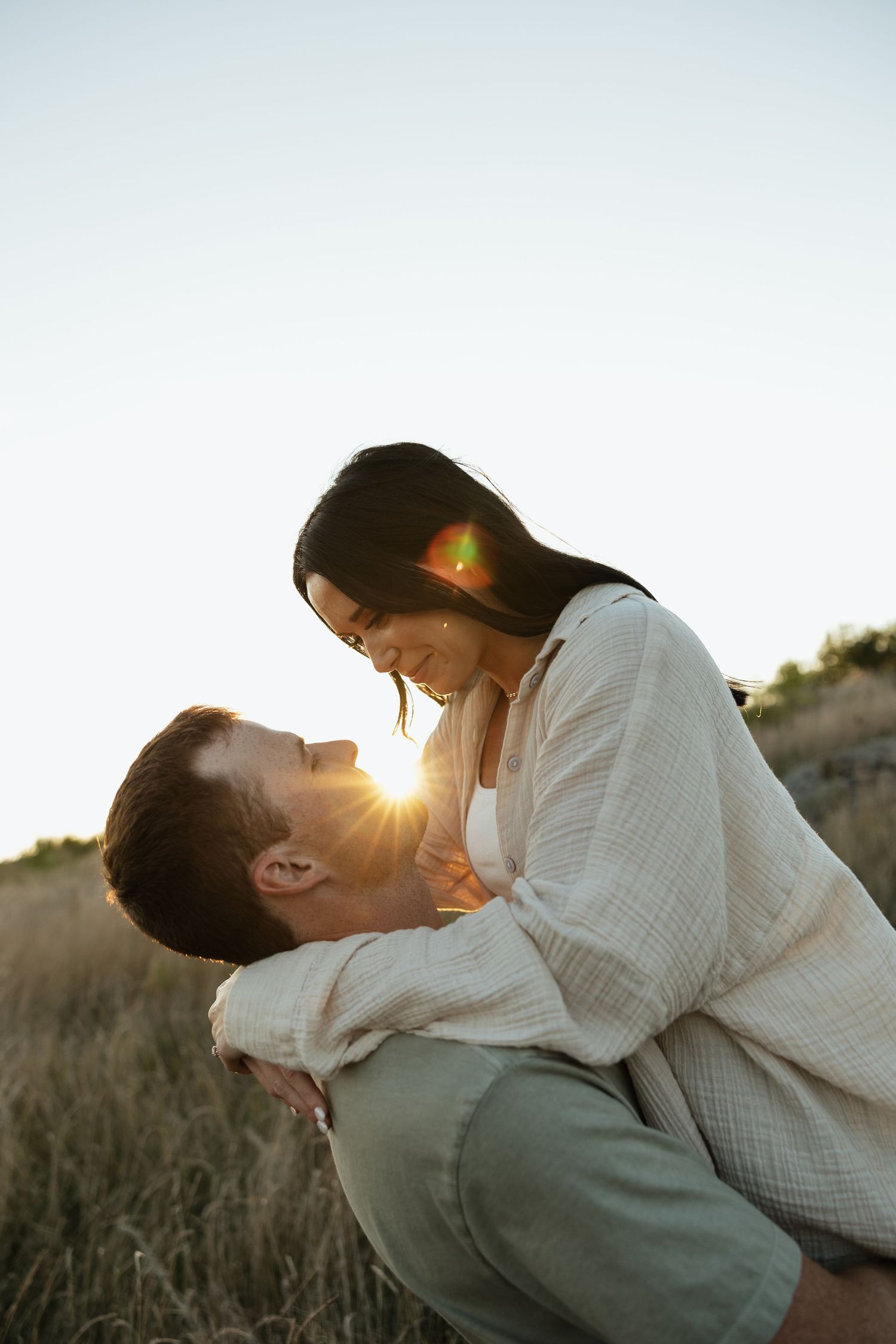 A romantic couple embraces in a golden field at sunset, creating a silhouette against the warm sky.